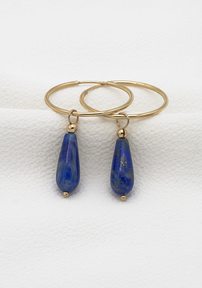 Lapislazuli Creolen aus 14k Gold Filled mit blauen Tropfenanhängern auf weißem Stoff drapiert. 