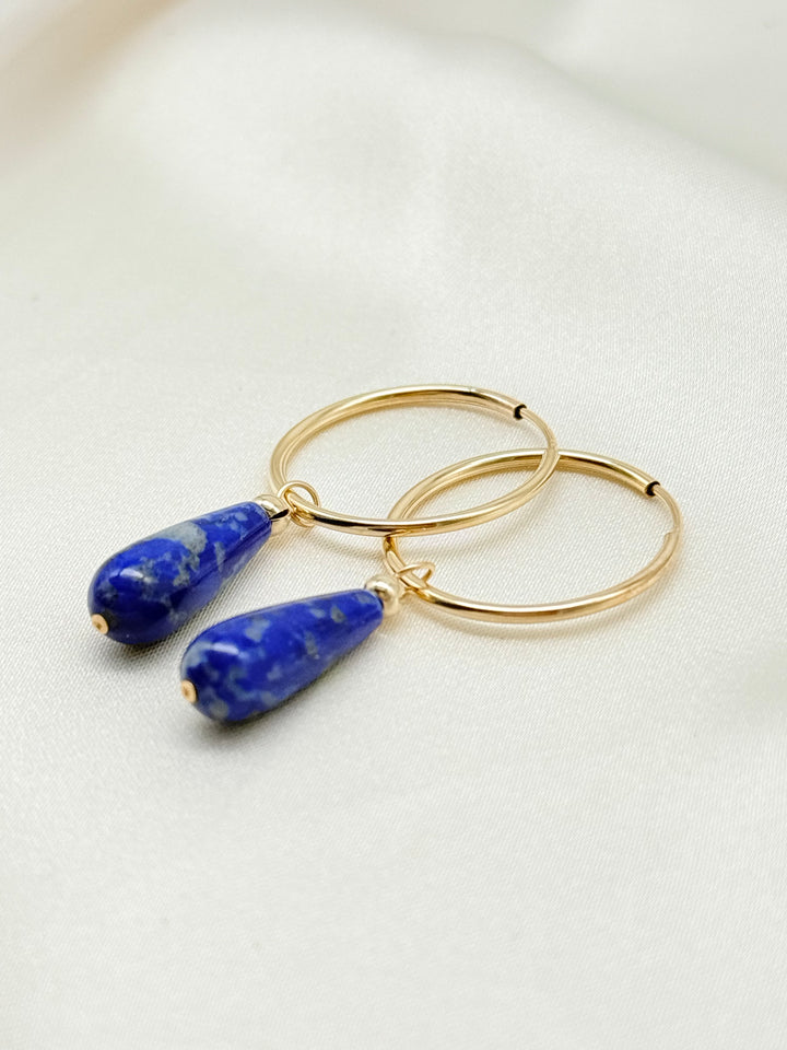 Lapislazuli Creolen aus 14k Gold Filled mit blauen Tropfenanhängern auf cremefarbenem Stoff.